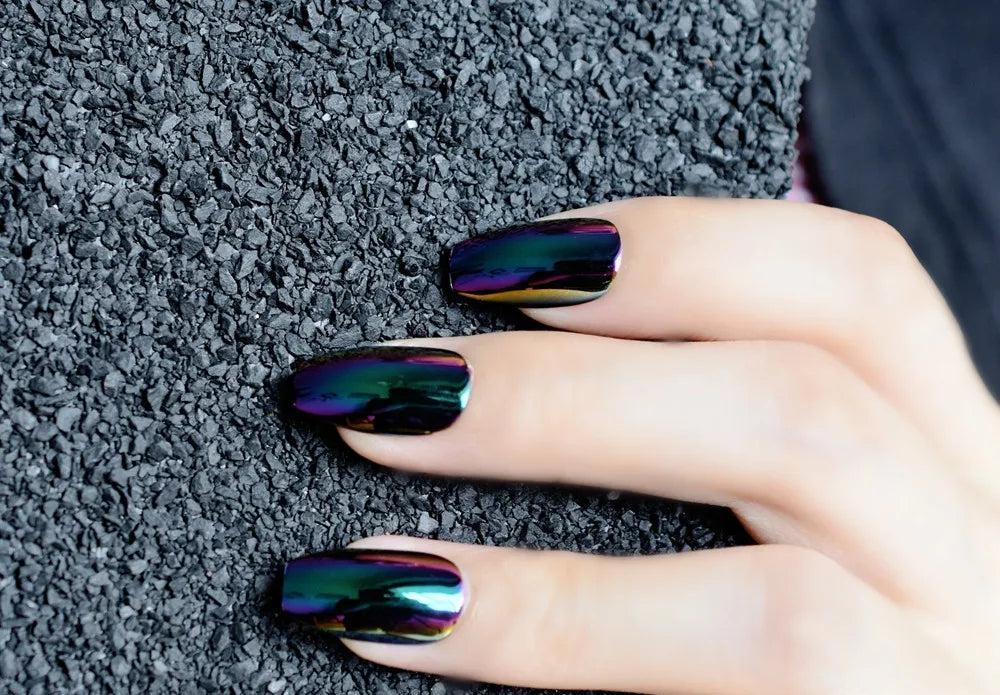 Hand with iridescent nail polish on a textured gray surface