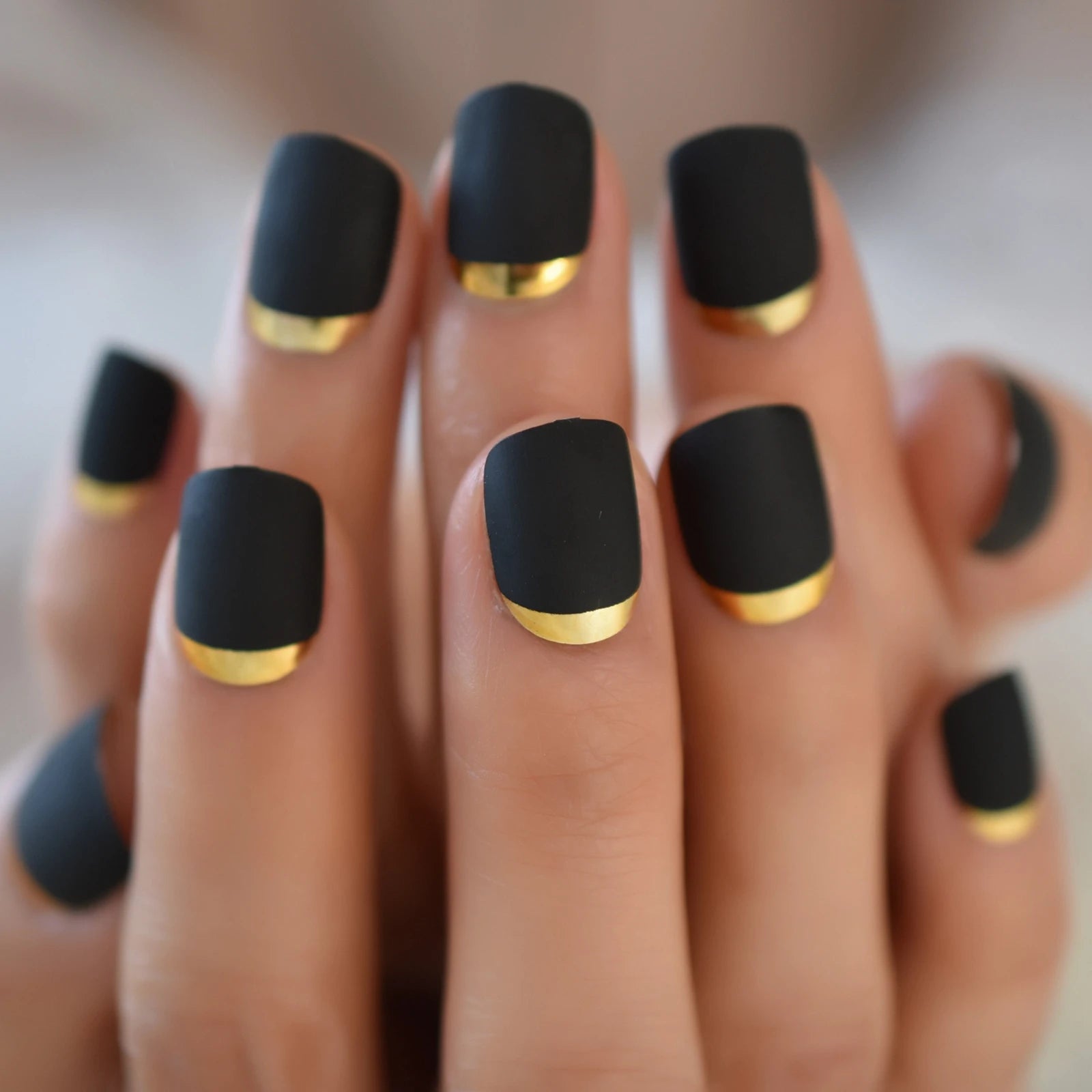 Black nails with gold accents on a blurred background