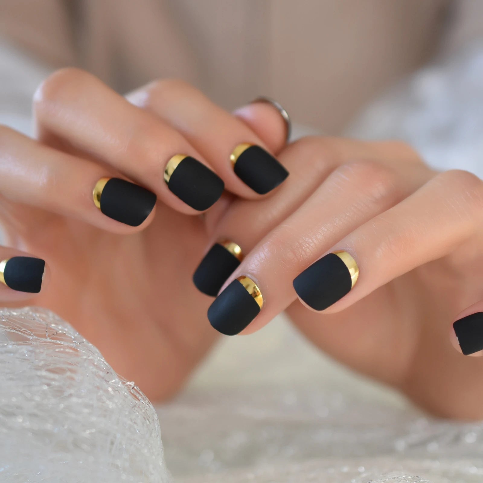 Close-up of hands with black nails and gold accents on a neutral background
