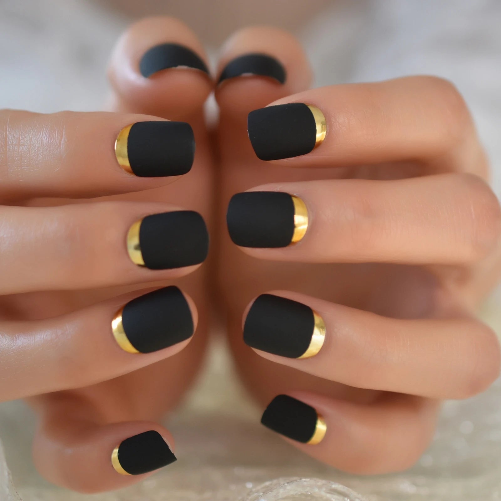 Black nails with gold accents on a neutral background