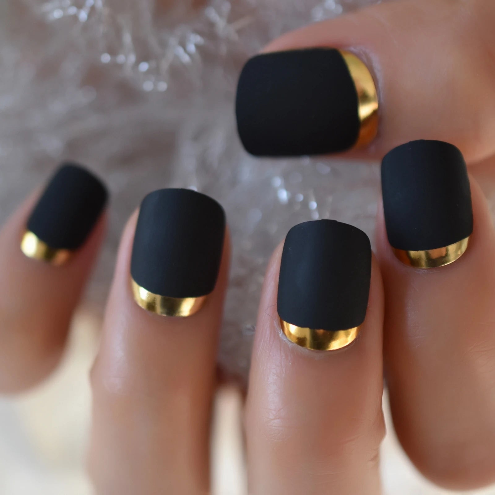 Black nails with gold accents on a textured white background