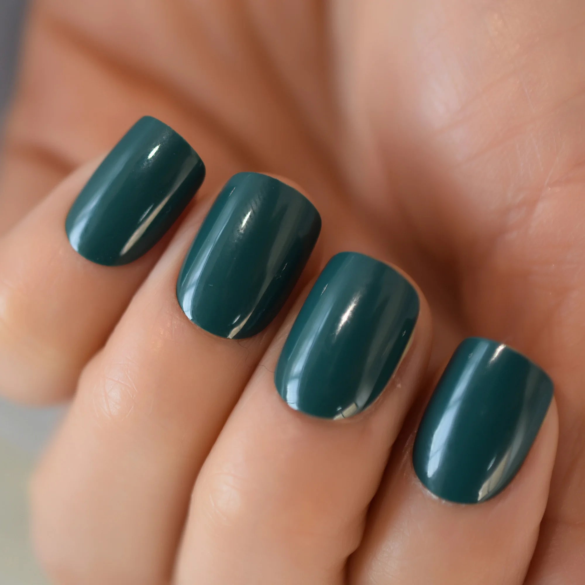 Close-up of a hand with teal nail polish on a neutral background