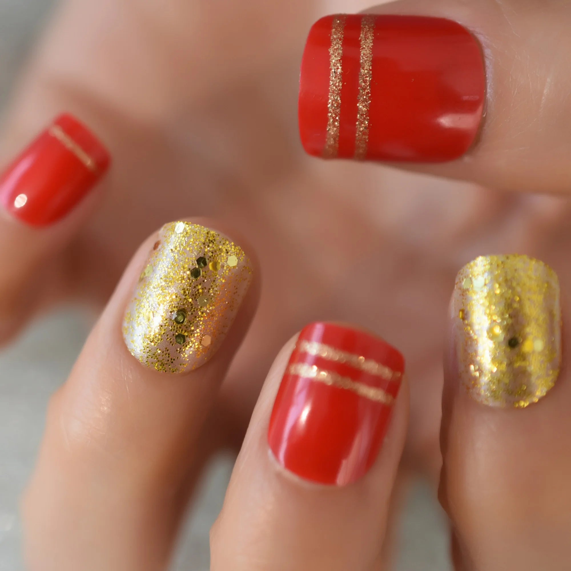 Close-up of a hand with red and gold nail polish on a blurred background