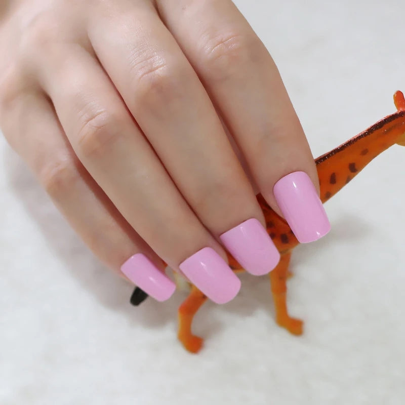 Hand with pink nail polish holding a small orange toy lizard on a white background
