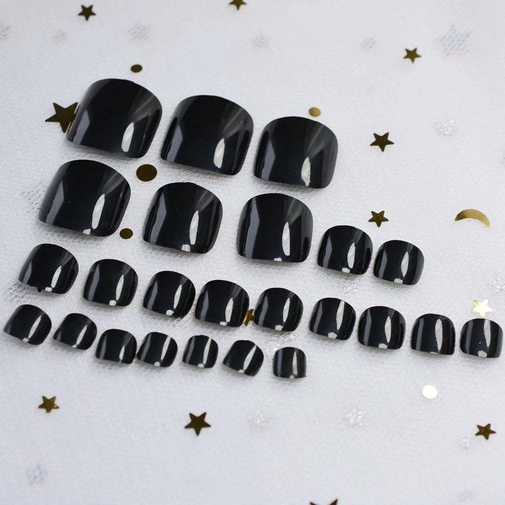 Set of black nail tips on a textured white surface with gold stars.