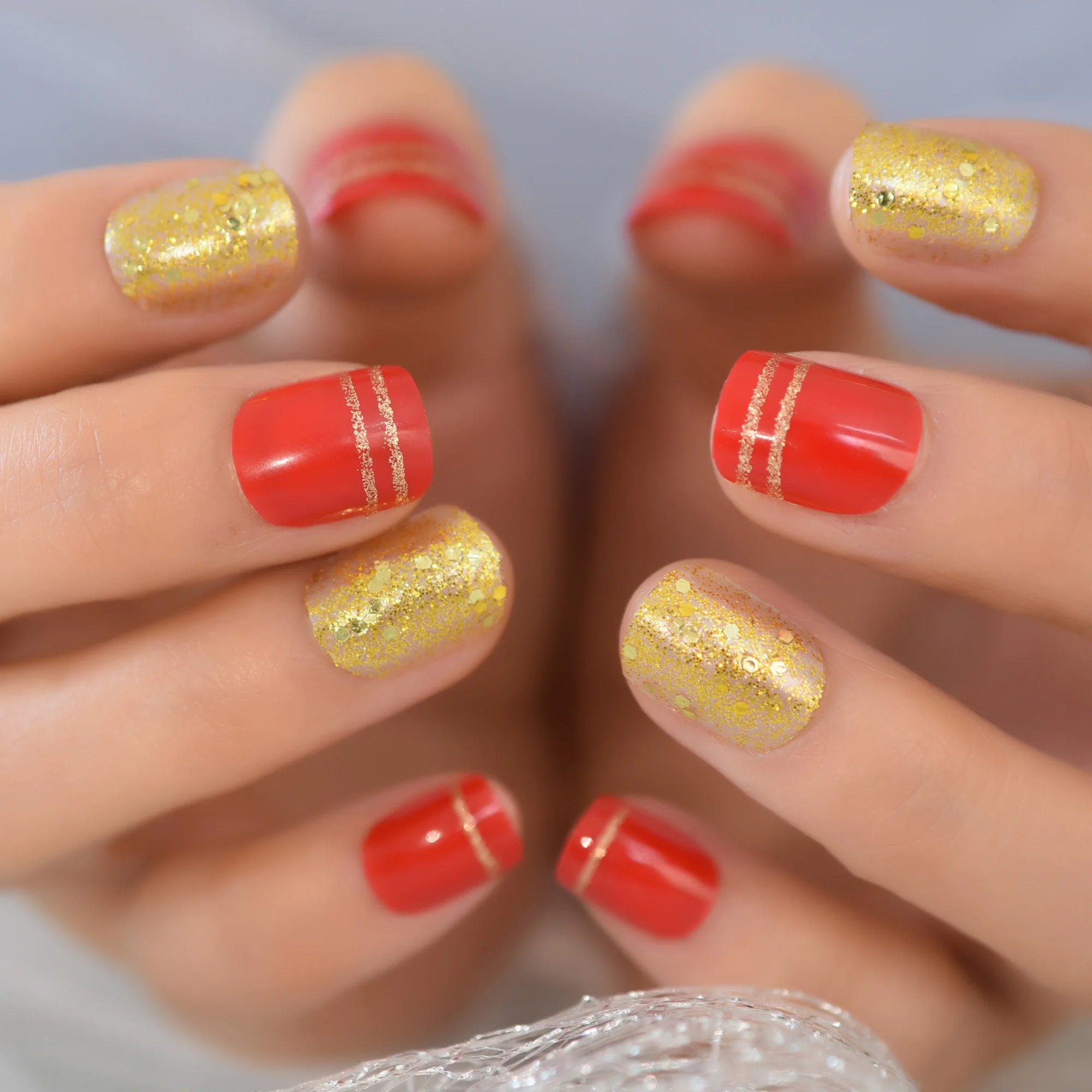 Close-up of hands with red and gold glittery nail polish on a neutral background