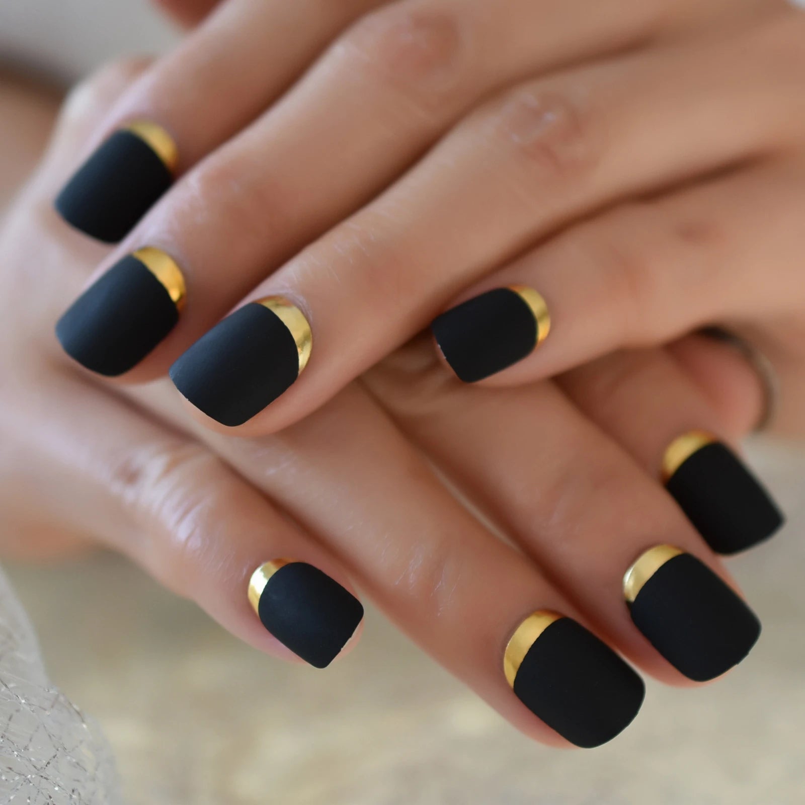 Close-up of hands with black nails and gold accents on a neutral background