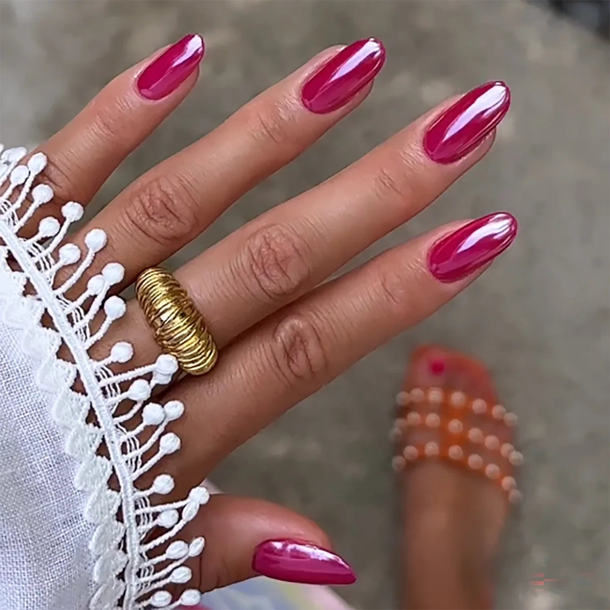 Hand with pink nails wearing a gold ring on a blurred background