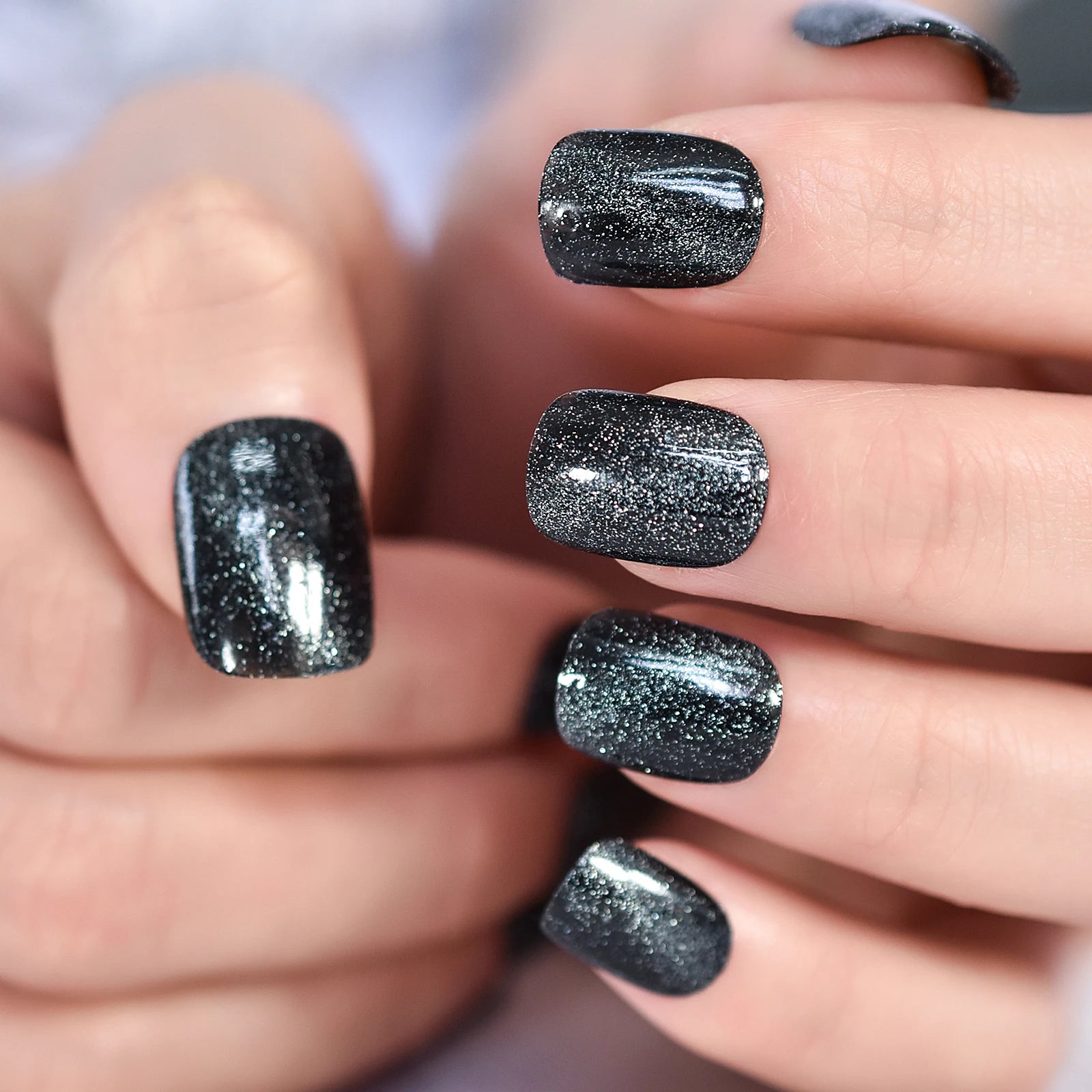 Close-up of a hand with black glittery nail polish on a blurred background