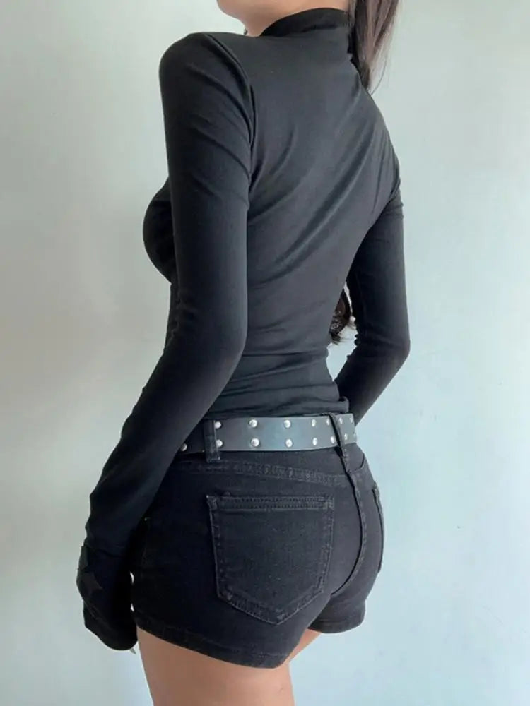 Person wearing a black long-sleeve top and black shorts with a studded belt on a plain background