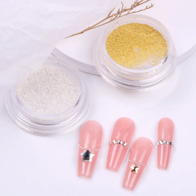Pink nail tips with decorative elements next to containers of gold and silver powder on a white background