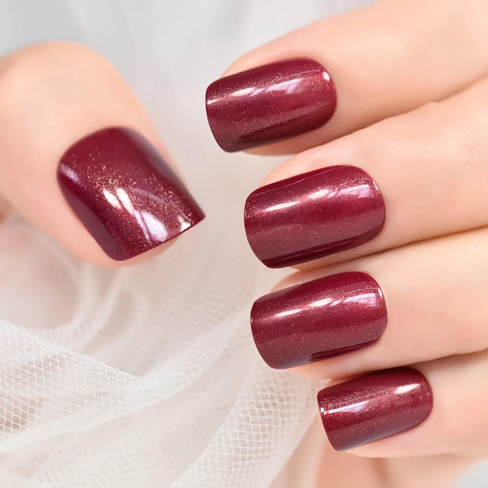 Close-up of a hand with burgundy glittery nail polish on a light background