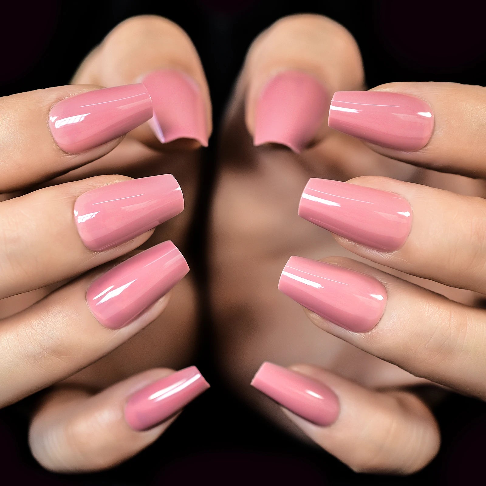 Close-up of hands with pink nail polish on a dark background