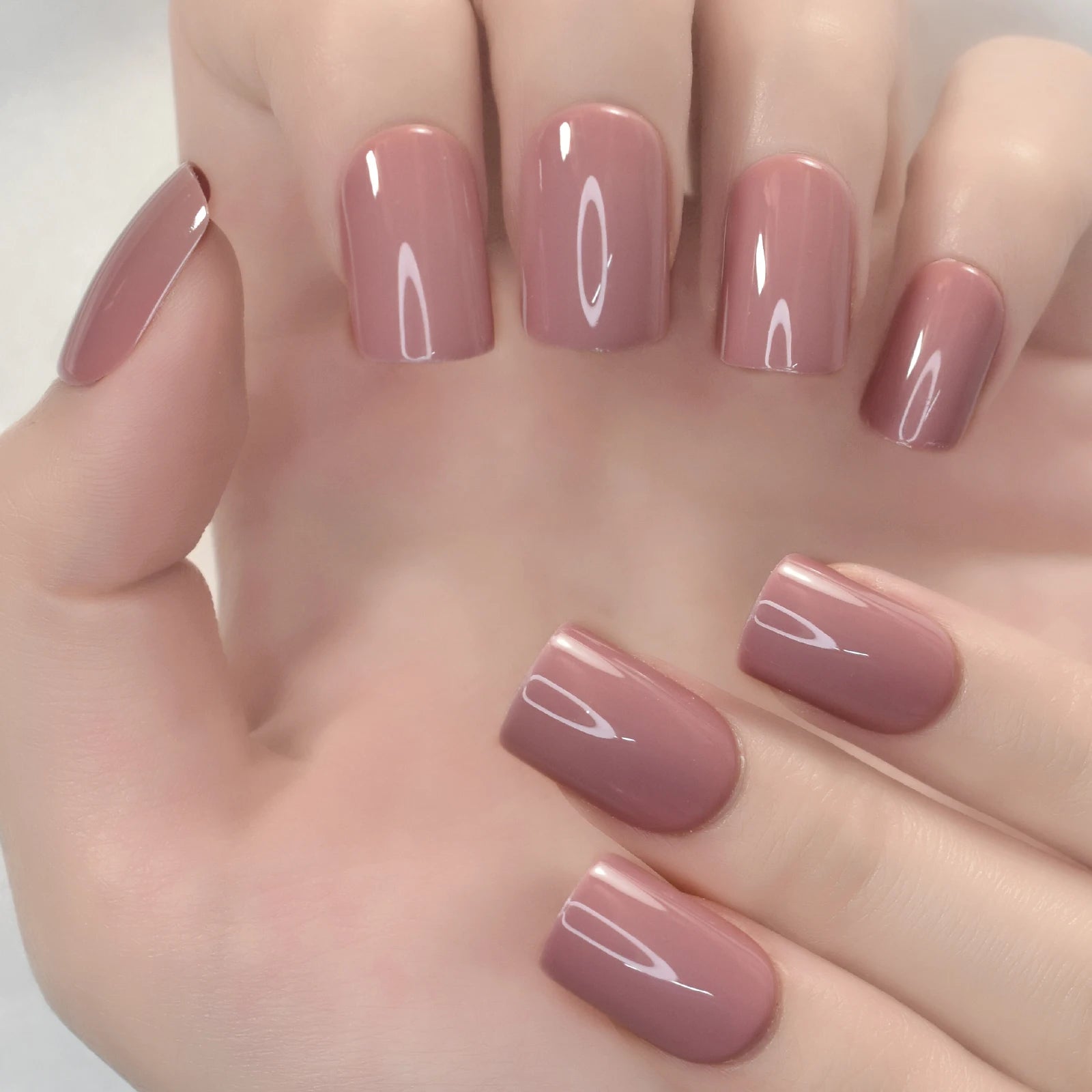 Hand with pink nail polish on a neutral background