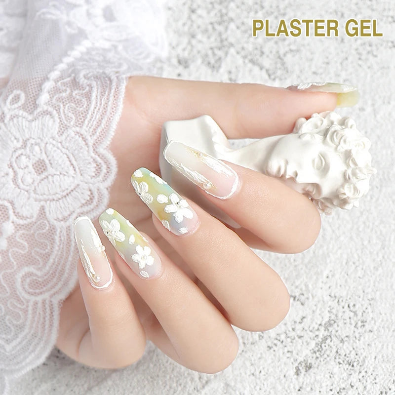 Hand with decorated nails holding a block of plaster gel on a textured white background