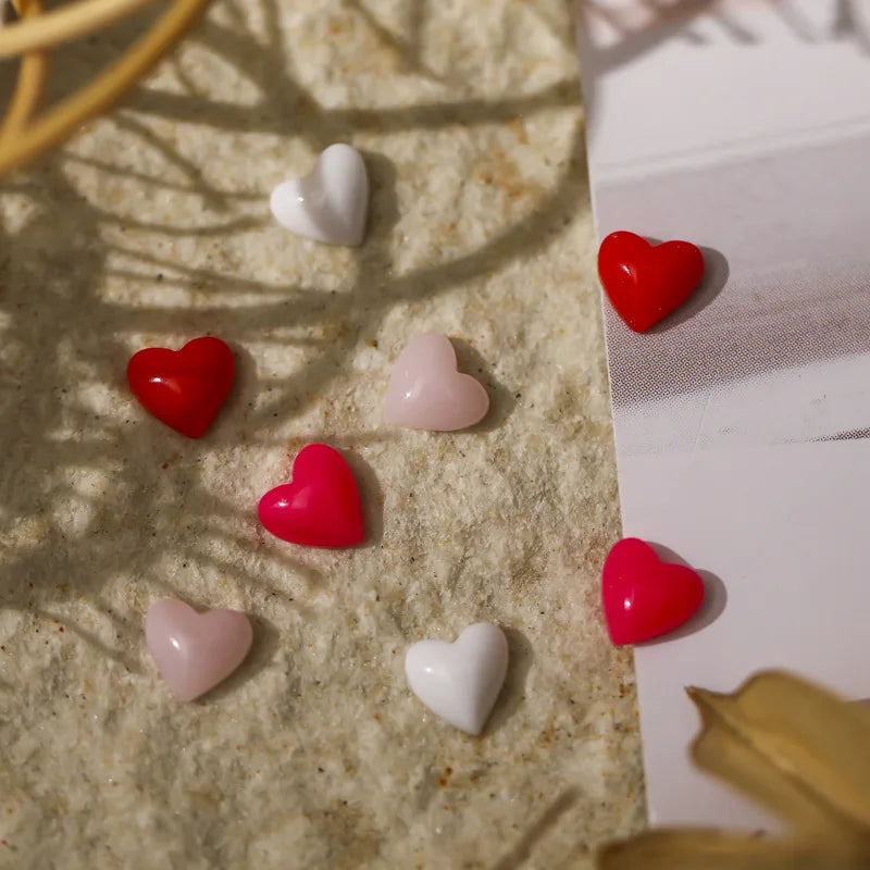 Heart-shaped objects in red, pink, and white on a textured surface with shadows.