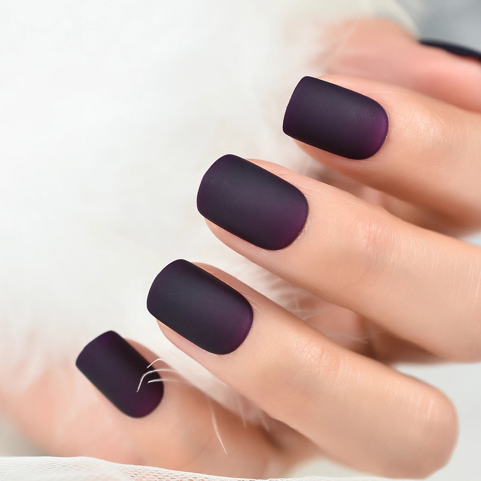 Close-up of a hand with dark purple nail polish on a white background
