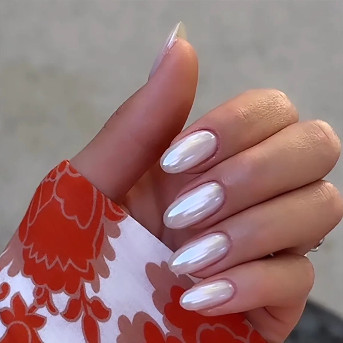 Close-up of a hand with white nail polish holding a red and white floral object.
