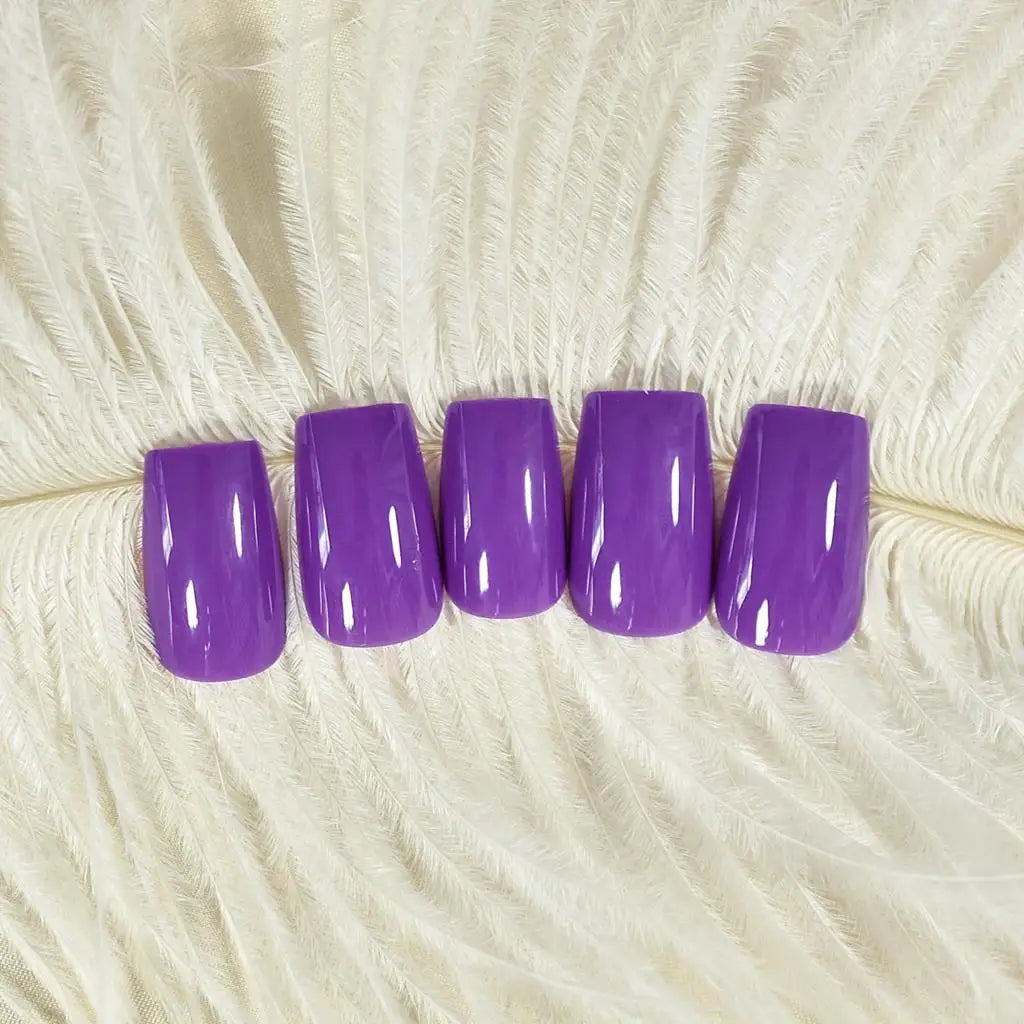 Five purple nail polish samples on a textured beige surface