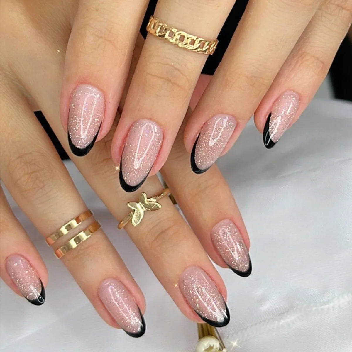 Close-up of hands with pink glittery nails and gold rings on a white background