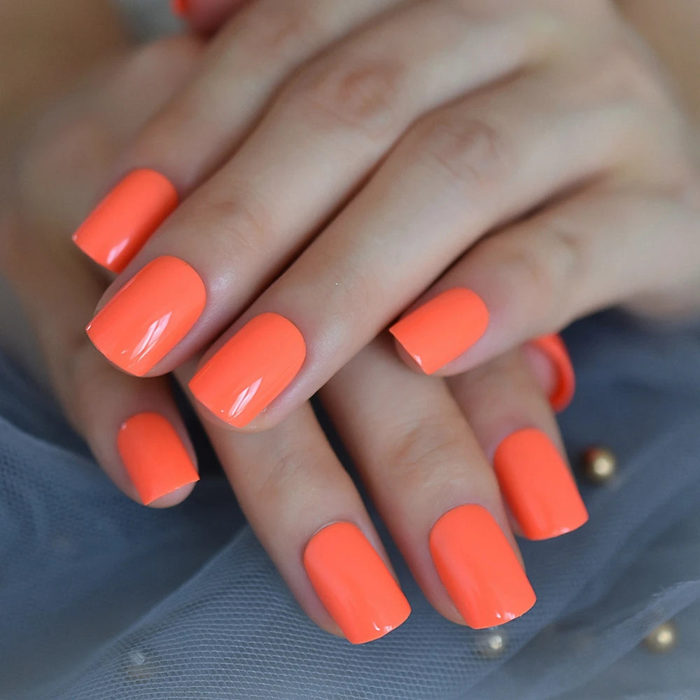 Close-up of hands with bright orange nail polish on a blurred background