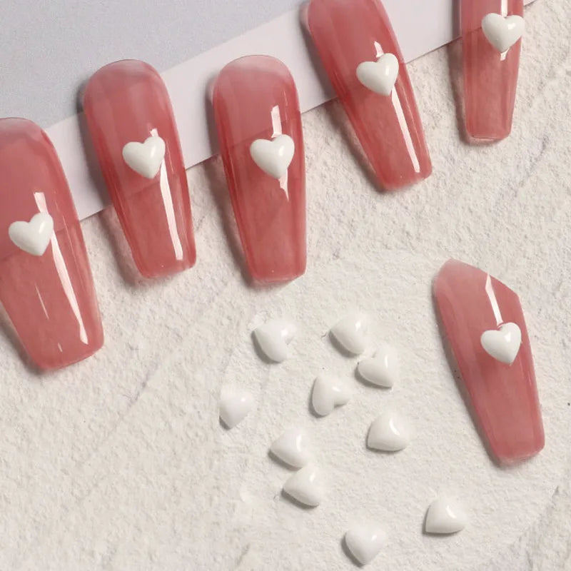 Nail art with white heart decorations on pink nail polish against a light background