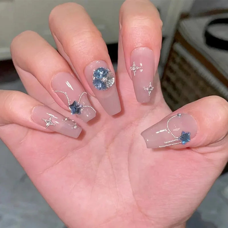 Hand with decorative nails featuring gemstones and jewelry-themed designs.