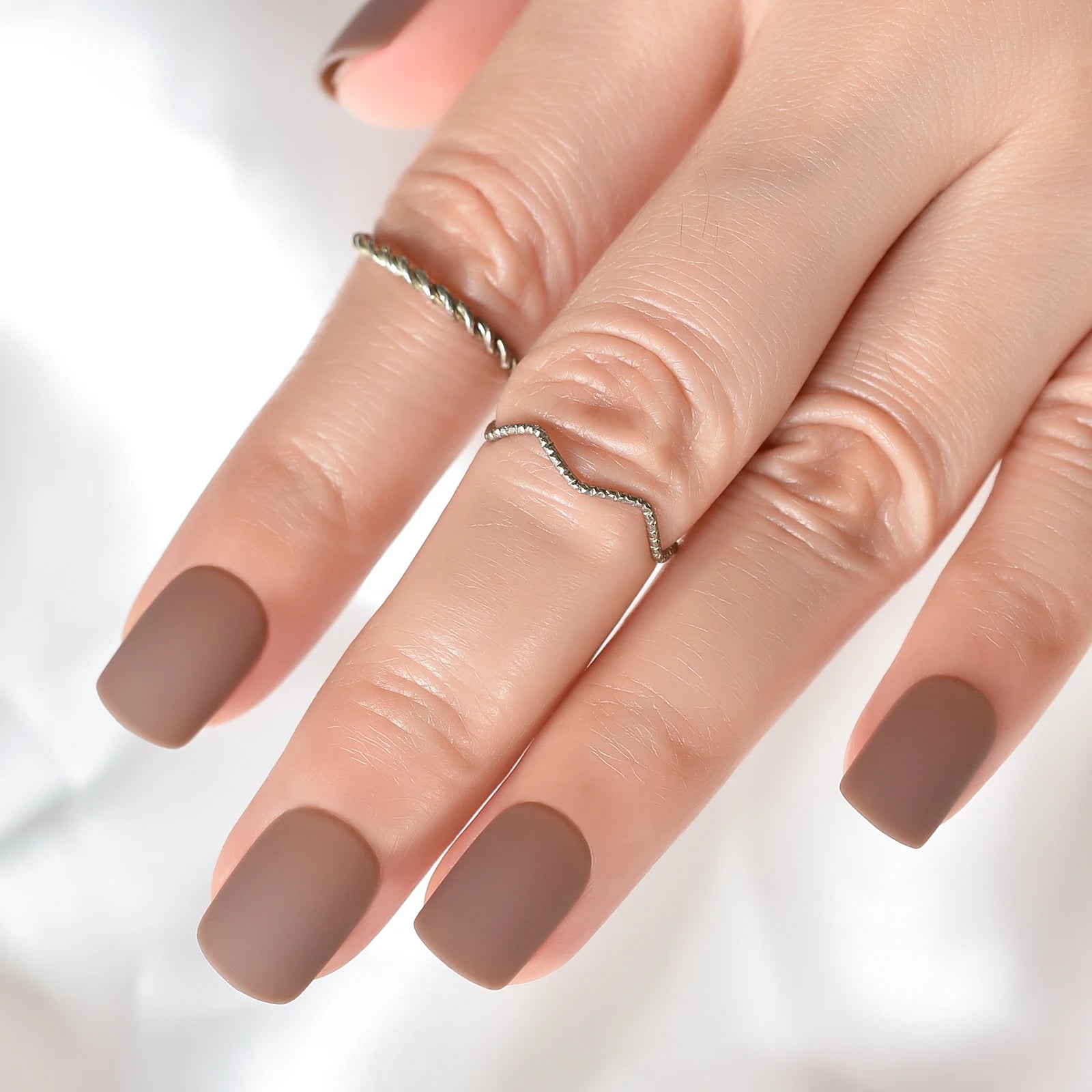 Close-up of a hand with brown nail polish on a light background