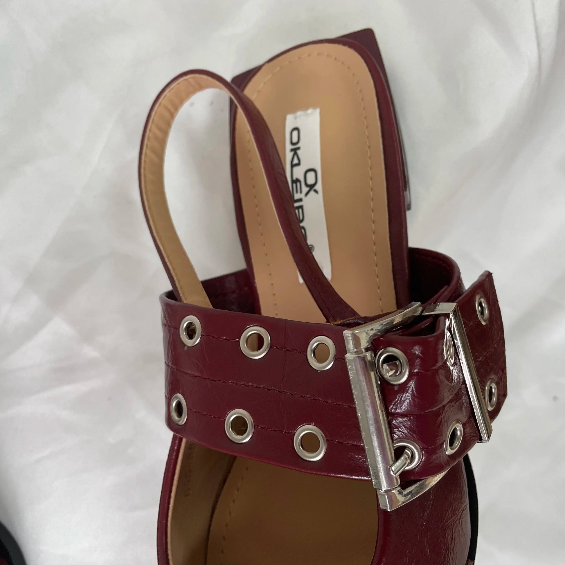 Maroon sandal with metal buckle and grommets on a white background