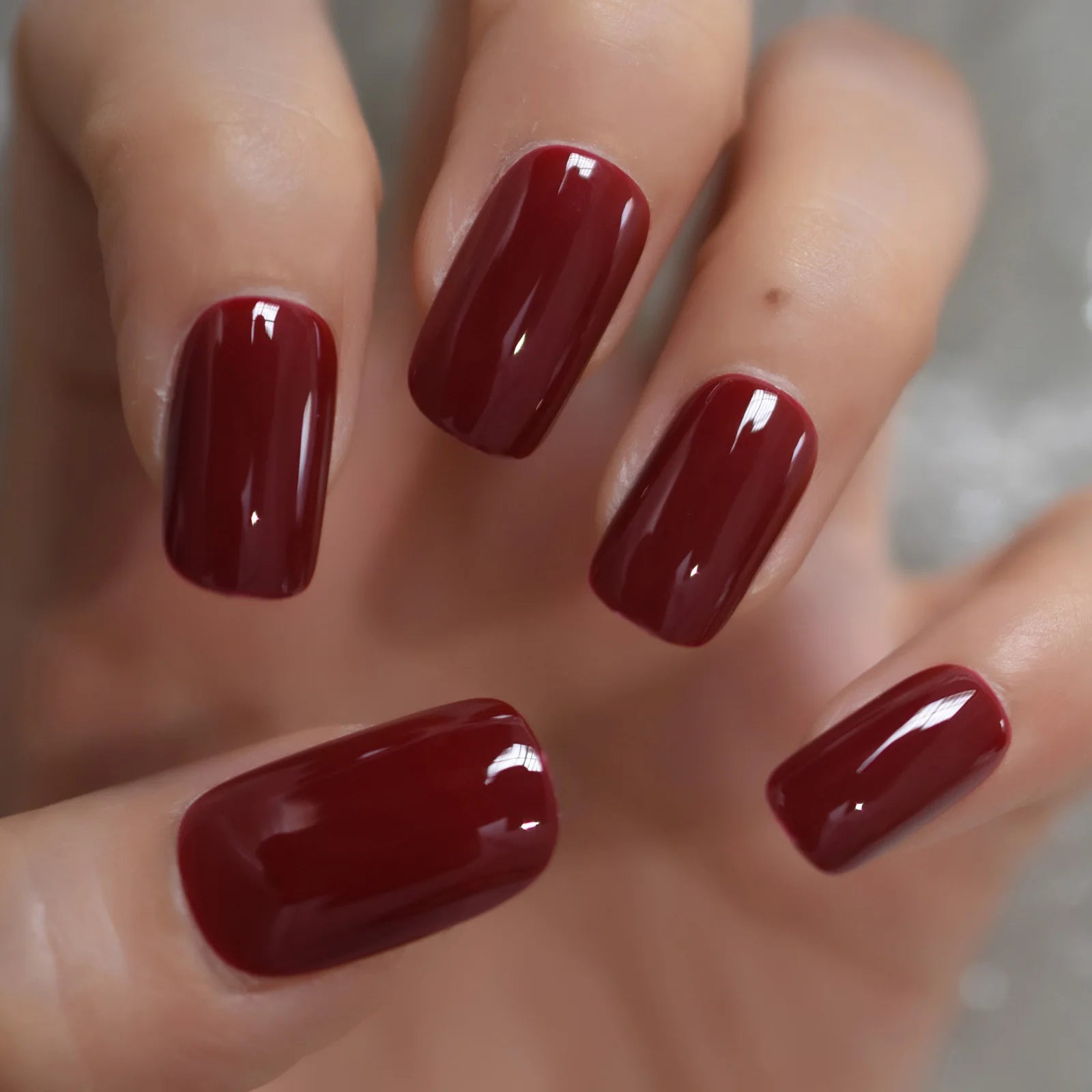 Close-up of a hand with dark red nail polish on a neutral background